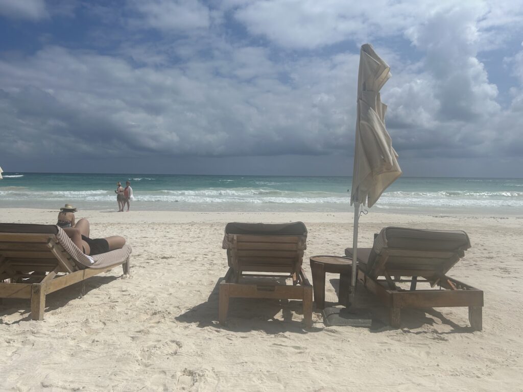 Wooden sunbeds with an umbrella on the sand facing the ocean