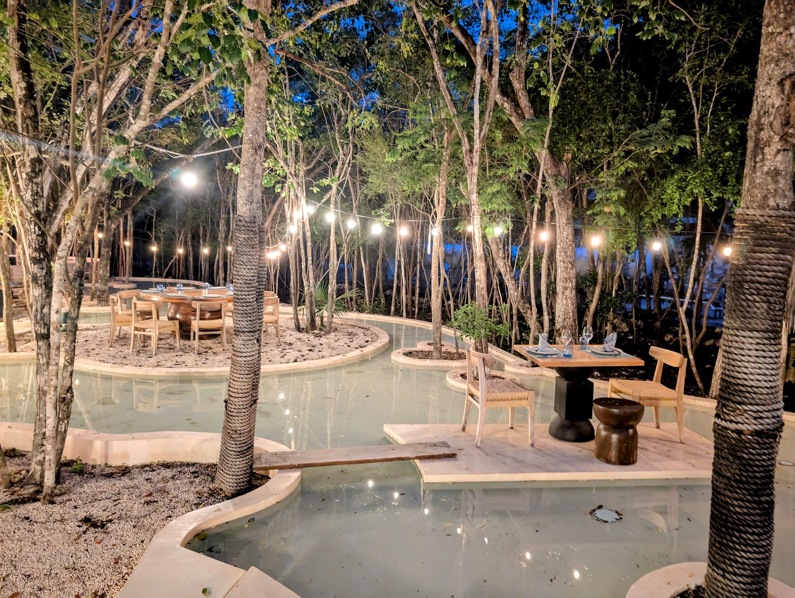 Outdoor event space lit with string lights among the trees