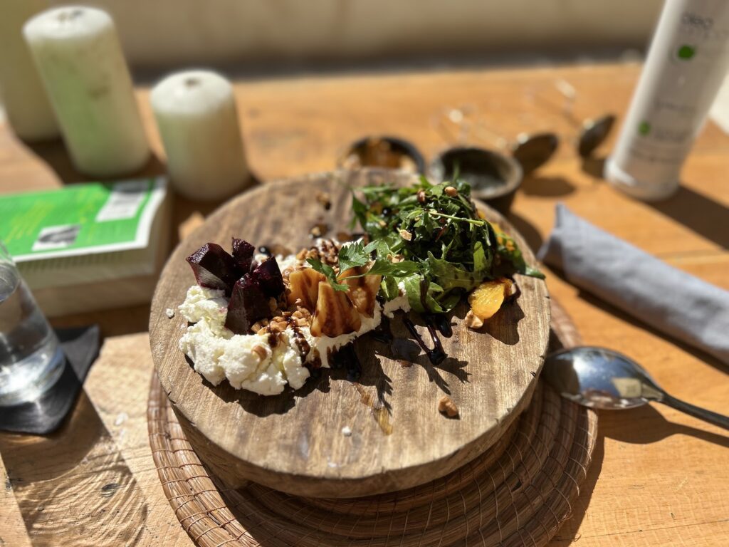 Plated starter with greens and cheese on a round wooden board