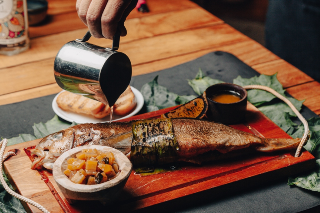 Server pouring sauce over a grilled fish dish