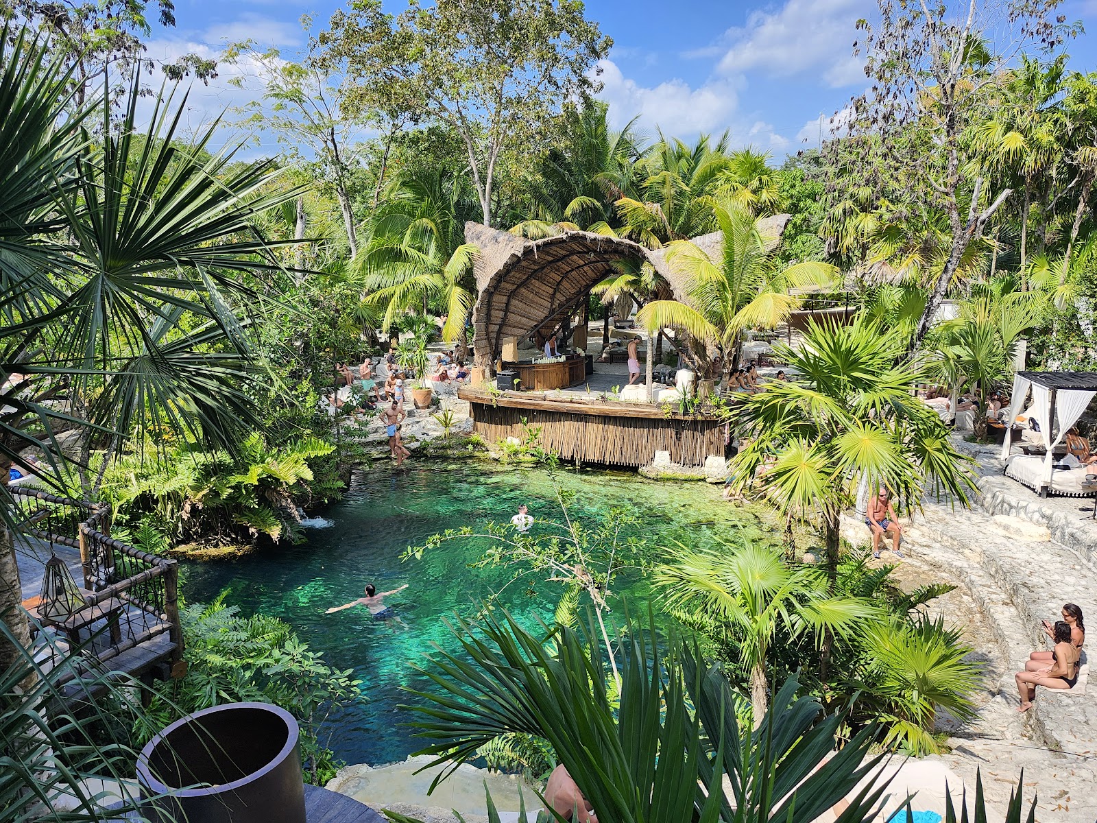 Vesica Tulum cenote framed by tropical plants and a palapa